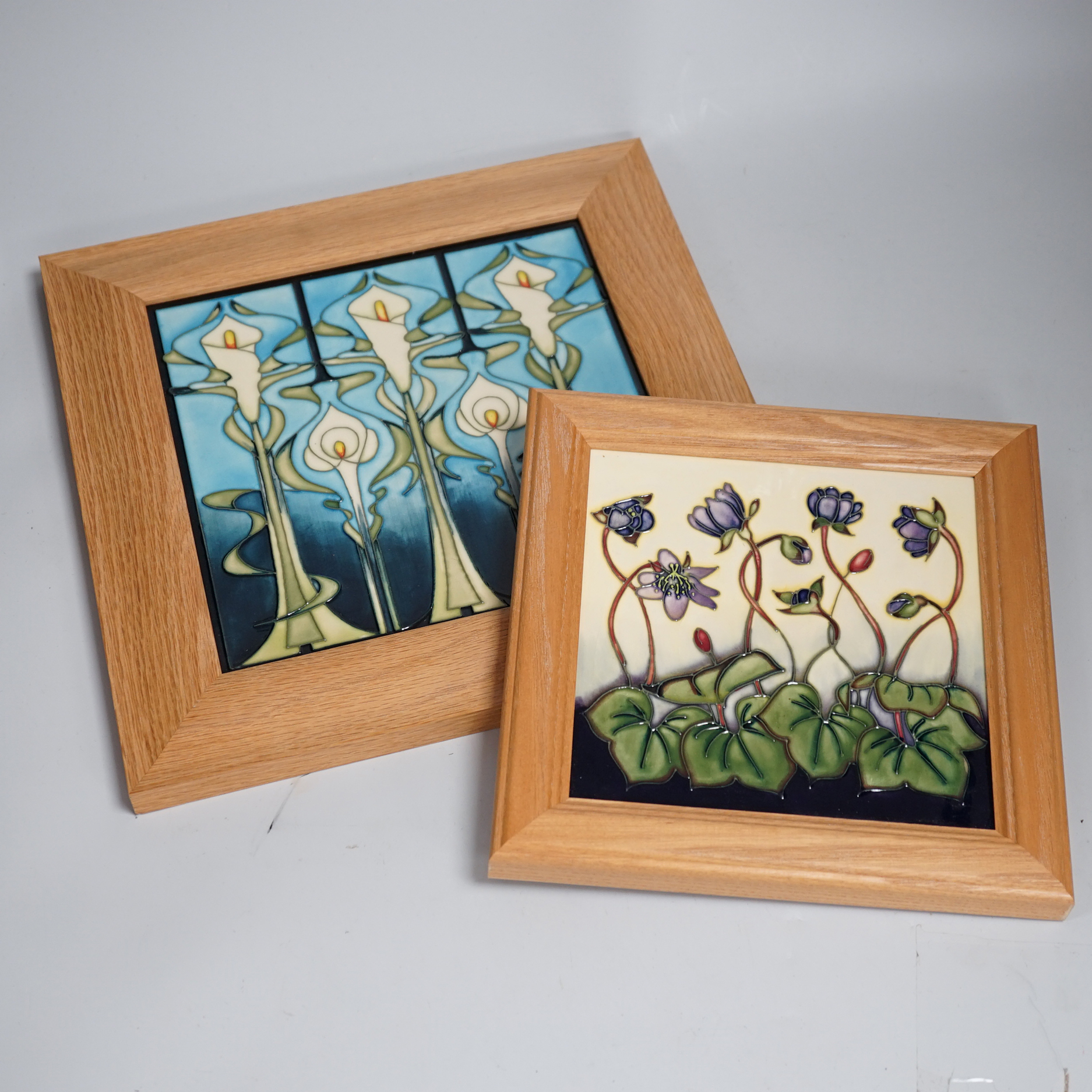Two framed Moorcroft tiles, one with stylised lilies, the smaller tile with cyclamen, larger tile 21.5cm x 21.5cm